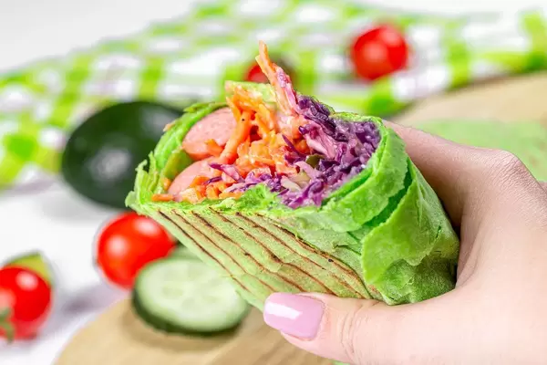 Fresh pita bread with purple cabbage, carrots, smoked sausages in hand, close-up (Flip 2020)