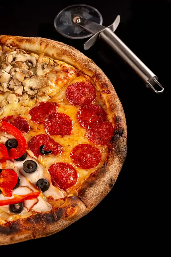 Fresh pizza with meat, smoked sausage, mushrooms and vegetables on a black background with a knife
