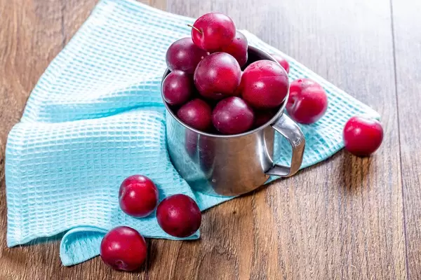 Fresh plums in an iron mug on the wooden background with a blue kitchen towel (Flip 2019)