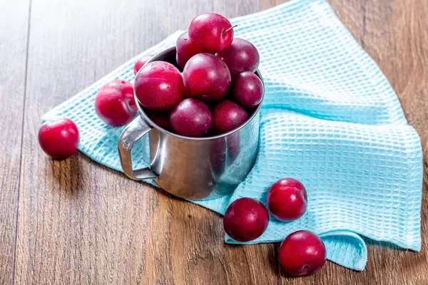 Fresh plums in an iron mug on the wooden background with a blue kitchen towel