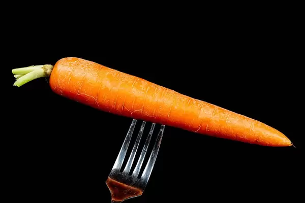 Fresh raw carrot on a fork on a black background