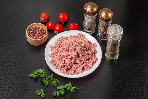 Fresh raw minced meat with spices, tomatoes and parsley on black background