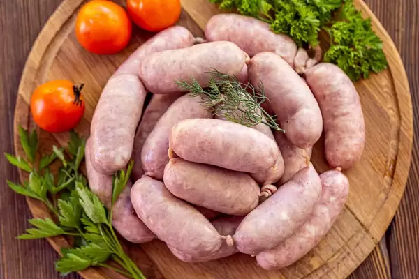 Fresh raw sausage on the wooden kitchen board, top view