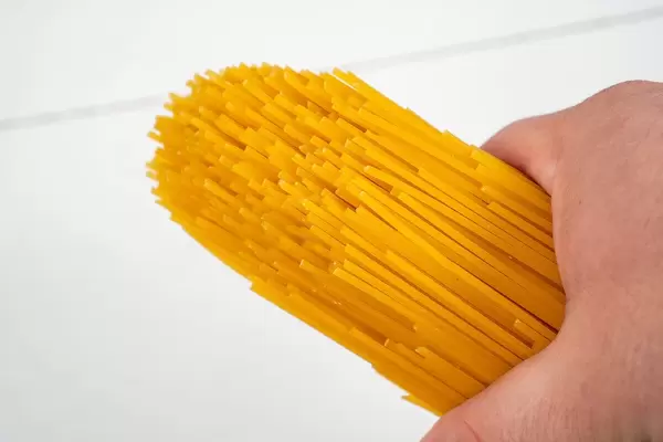 Fresh Raw Spagheti in the hand above white wooden background (Flip 2020)