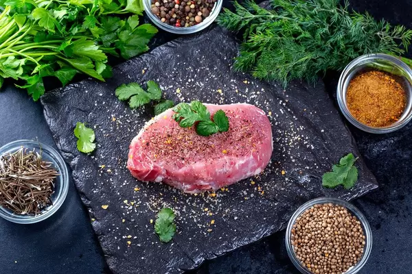 Fresh raw steak with spices and herbs on a black stone background