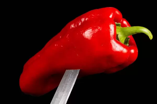 Fresh red bell pepper on a knife, close-up