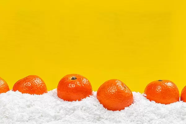 Fresh ripe tangerines on snow with yellow background behind with free space (Flip 2019)