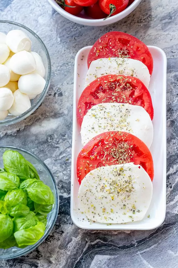 Fresh ripe tomatoes, mozzarella and young green Basil leaves on grey stone background