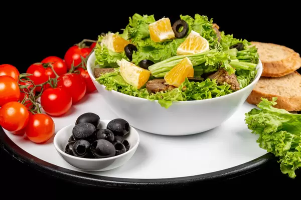 Fresh salad with lettuce, black olives, orange slices and liver, healthy food background