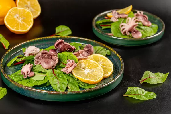 Fresh salad with pickled octopus, beet leaves and lemon, dark background