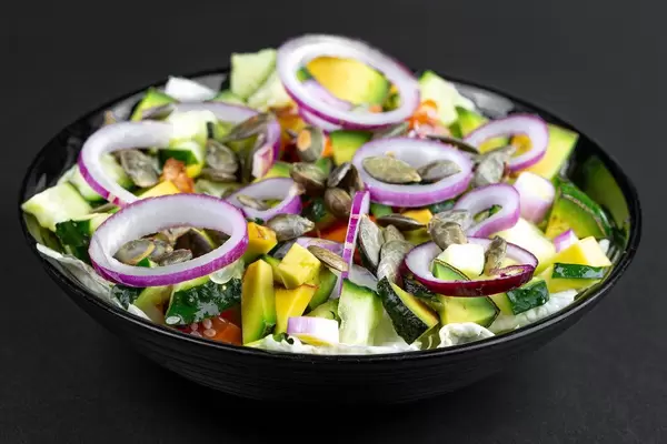 Fresh salad with sliced vegetables, purple onion rings and pumpkin seeds