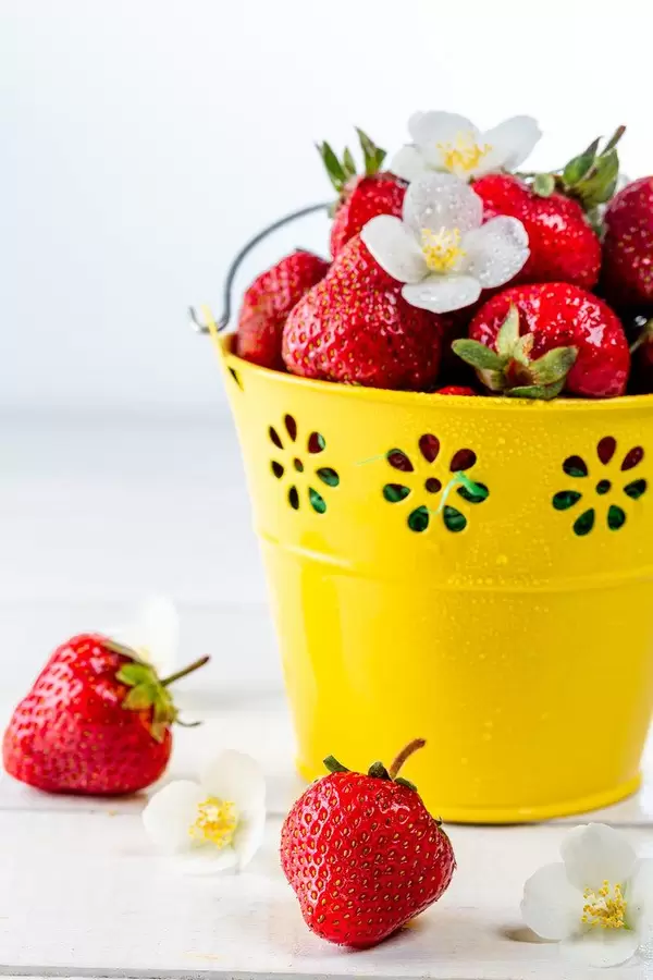 Fresh strawberries with white flowers in a yellow bucket on a wooden table