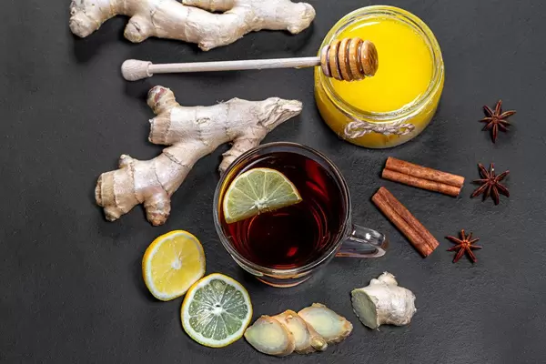 Fresh tea with honey, lemon, ginger root, cinnamon sticks and anise star on black background