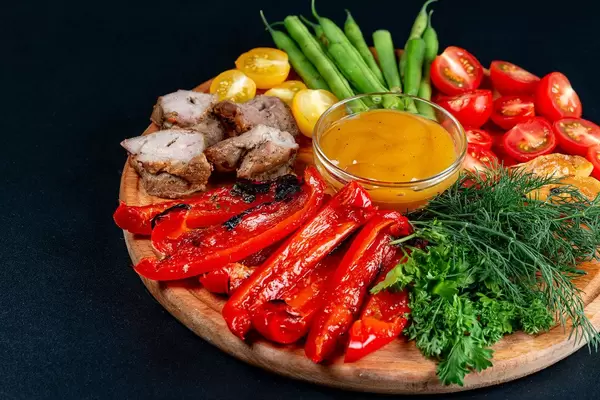 Fresh vegetables and greens with grilled vegetables and meat on a black background