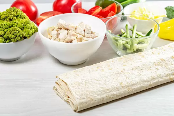 Fresh whole and sliced vegetables with chicken fillet and pita on the kitchen table (Flip 2019)