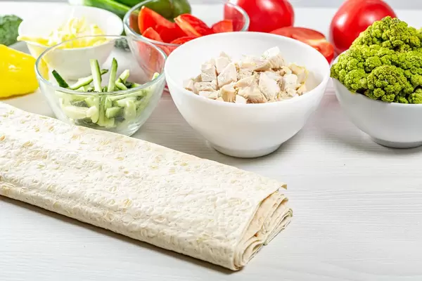 Fresh whole and sliced vegetables with chicken fillet and pita on the kitchen table