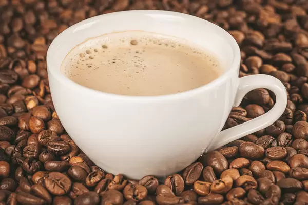 Freshly brewed espresso in a white cup on a background of coffee beans