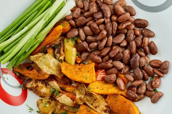Freshly fried vegetables with boiled haricot beans and green onions on the plate