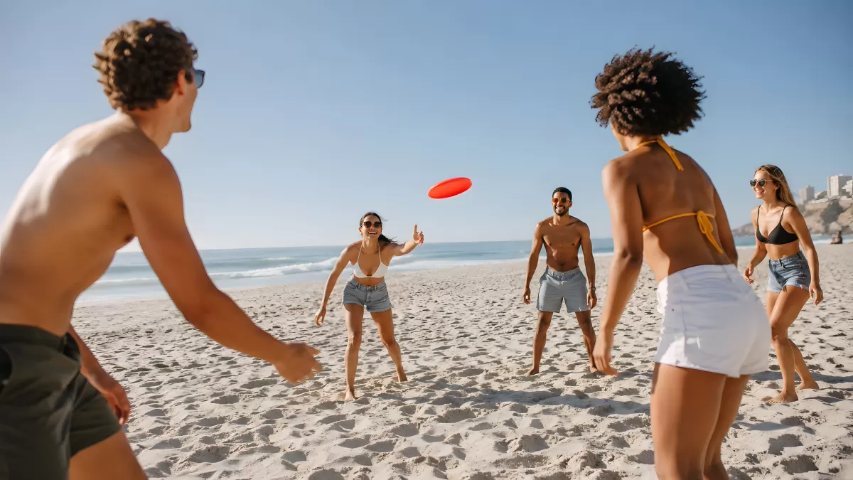 Freunde spielen Frisbee am sonnigen Sandstrand