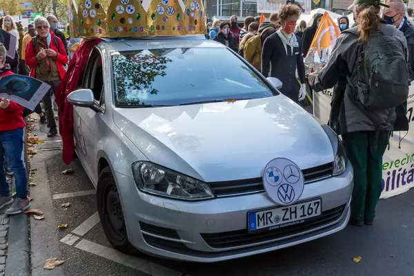Fridays for Future Demonstranten mit Maske und ein Auto mit Krone und BMW, Mercedes und VW Logos