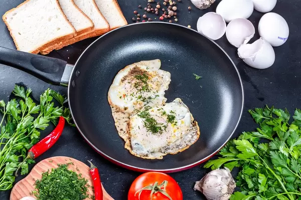 Fried chicken eggs with greens in a frying pan