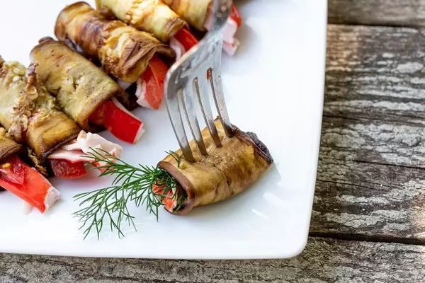 Fried eggplant with tomatoes and crab sticks with fork