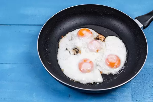 Fried Eggs in the black frying pan above wooden table