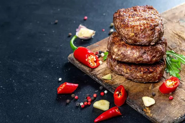 Fried meat cutlets with pieces of chili and garlic on an old kitchen Board on a black background (Flip 2019)