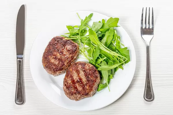 Fried meat patties and arugula on a white plate with a knife and fork (Flip 2019)