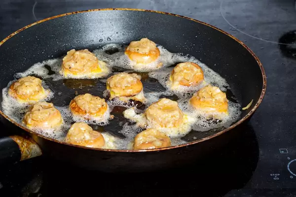 Fried stuffed bagels in a frying pan on an electric hob
