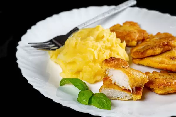 Fried tilapia fillet with basil leaves and potatoes, close-up