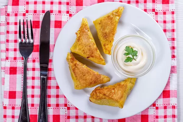 Fried triangles with minced meat inside on a white plate with sauce (Flip 2019)