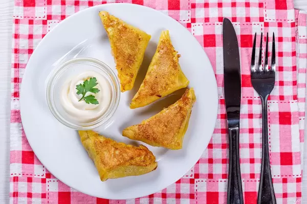 Fried triangles with minced meat inside on a white plate with sauce