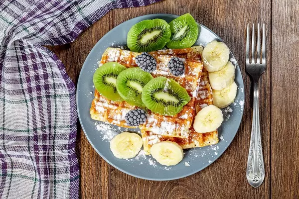 Fried waffles with kiwi, banana and powdered sugar. Top view (Flip 2019)