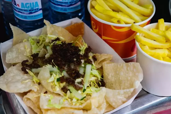 Frisch frittierte Nachos mit Salat, Gurke und Pommes Frites auf einem Papierteller