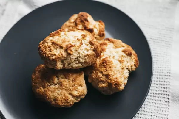 Frisch gebackene englische Scones (Gebäck) auf dunklem Teller auf weißem Tischtuch