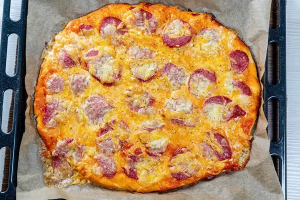 Frisch gebackene hausgemachte Pizza mit Wurst und Käse auf einem schwarzen Backblech