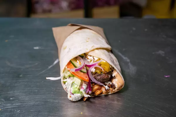 Frisch zubereiteter Döner Dürum mit Lamm, Zucchini, Zwiebeln, Tomaten, Gurken, Tzatziki, Cocktail Soße, Salat und Käse auf einer Küchen-Arbeitsfläche