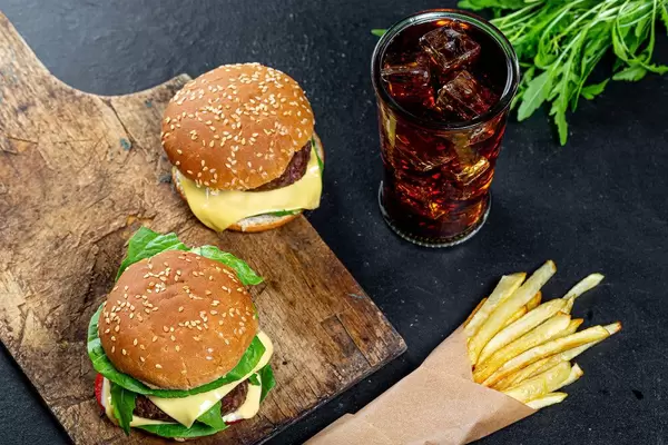 Frische Burger, eisgekühlte Cola und verpackte Pommes, auf einem dunkeln Küchentisch