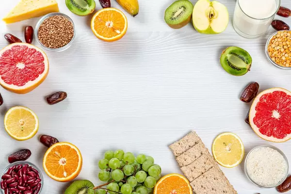Frische Früchte, Getreide, Milchpulver und Brot auf einem weißen Holzhintergrund mit Freiraum in der Mitte