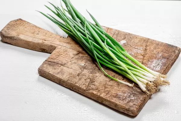 Frische Frühlingszwiebeln auf einem alten Holzschneidebrett vor weißem Hintergrund