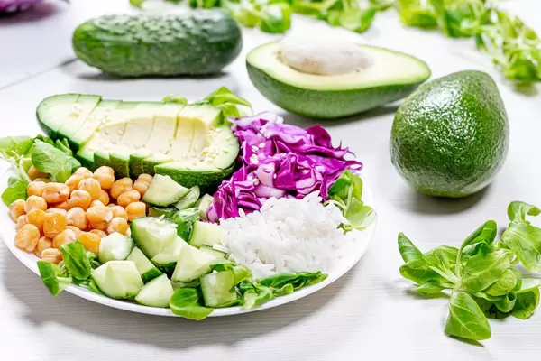 Frische Gurken, geschnittene Avocado mit Schale und Rotkohl, Maissalat mit weißem Reis und Kichererbsen