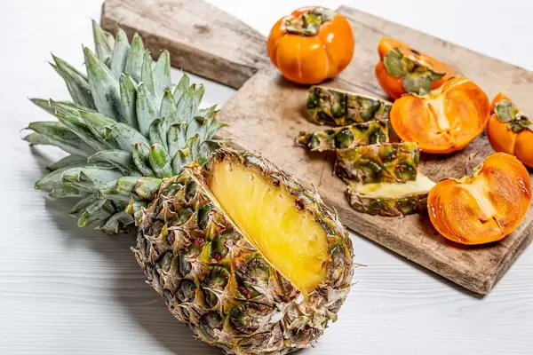 Frische Kaki und Ananas - aufgeschnitten auf einem alten Holzschneidebrett