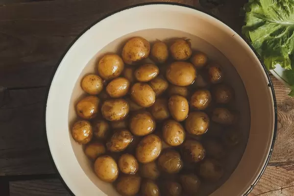 Frische, kleine Kartoffeln im Wasser in einem Kochtopf auf rustikalem Holztisch