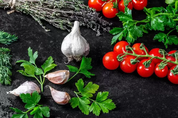 Frische Kräuter wie Thymian, Dill und Petersilie, auf einem schwarzen Hintergrund, mit Tomatenstränge und Knoblauchzehen