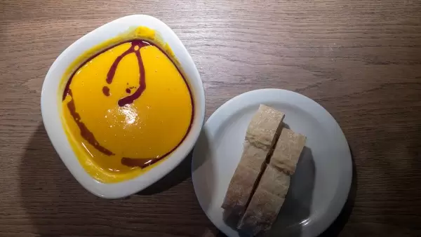 Frische Kürbissuppe Vapiano mit zwei Scheiben Ciabatta-Brot auf Holzunterlage - Nahaufnahme in Draufsicht