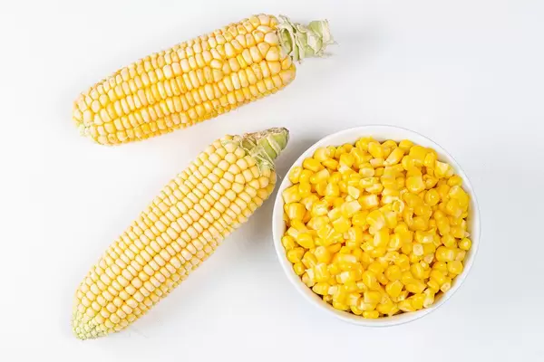 Frische Maiskolben und eine Schüssel Maiskörner. Aufnahme von oben