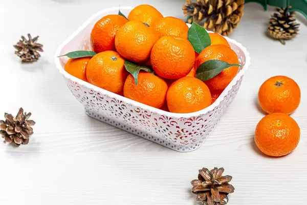 Frische Mandarinen in einem weißen Korb mit Zapfen daneben