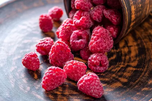 Frische, pinke Himbeeren liegen verteilt auf einem braunen Holzteller