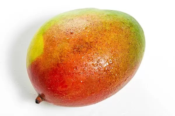 Frische, reife Mango mit Wassertropfen auf weißem Hintergrund
